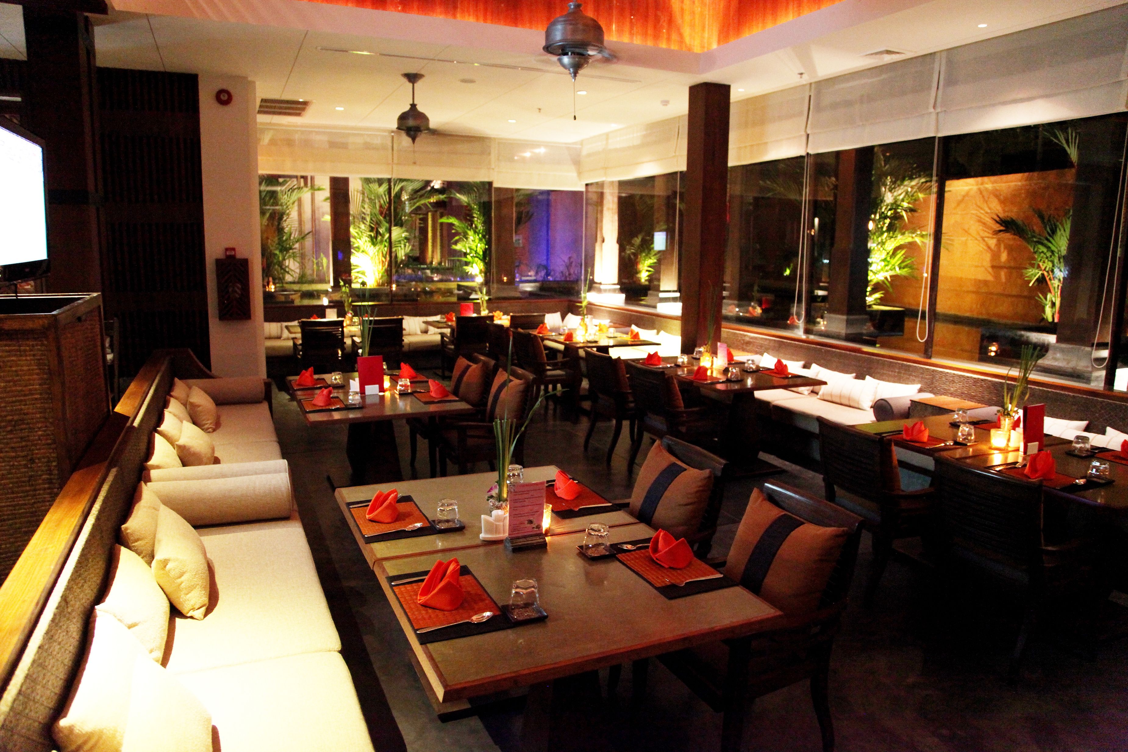 A restaurant with a long dining table, multiple chairs, and a sofa. There are plants and candles on the tables.