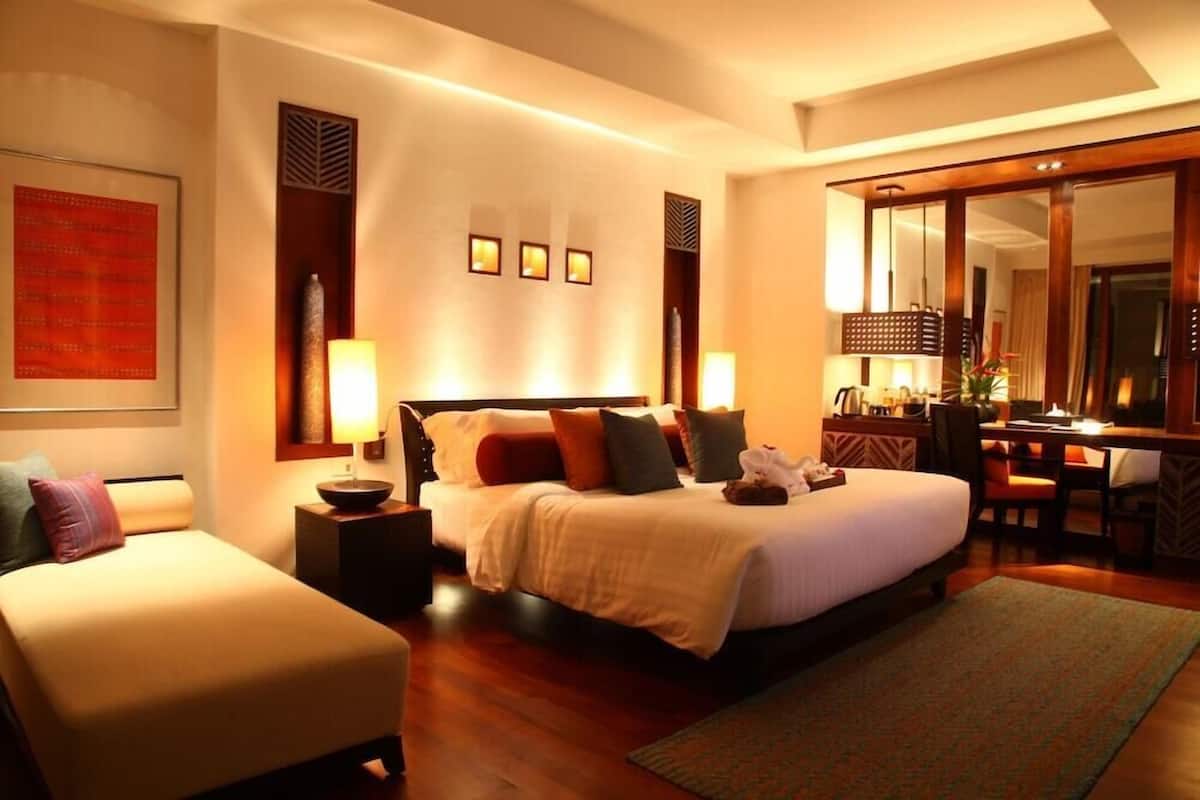 A hotel room with a large bed, a desk, and a chair. There are wall-mounted lights and a large mirror.