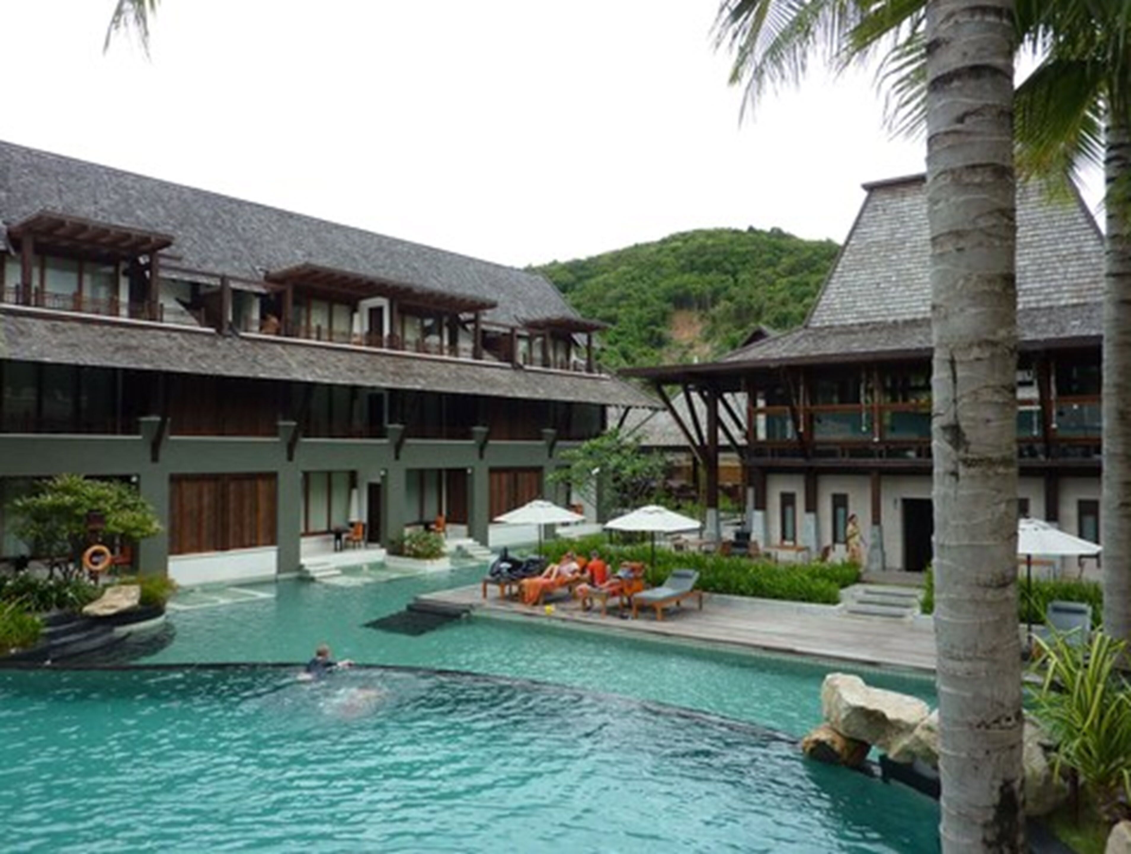 A resort with a swimming pool, multiple guest rooms, and a lush green landscape.