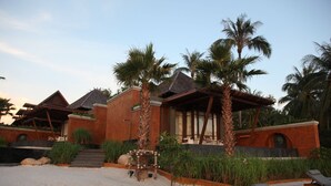 Un complexe hôtelier comprenant plusieurs bâtiments de style bungalow, des palmiers et une plage de sable fin avec des chaises longues.