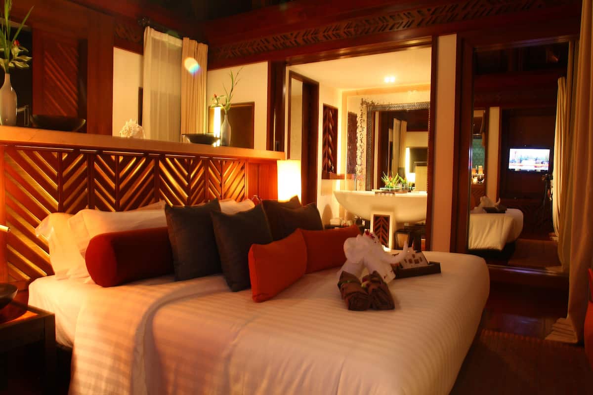A hotel room with a bed, a nightstand, a mirror, a TV, and a bathroom visible through an open door.