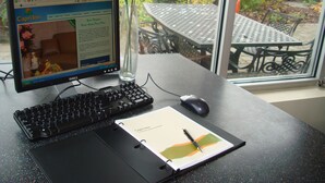 A computer monitor displaying a hotel website, a keyboard, a mouse, a notepad with a pen, and a vase with flowers. - Capri Inn (St. Catharines)