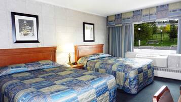 A hotel room with two beds, a nightstand, a lamp, framed pictures on the wall, and a window with a view of a park.