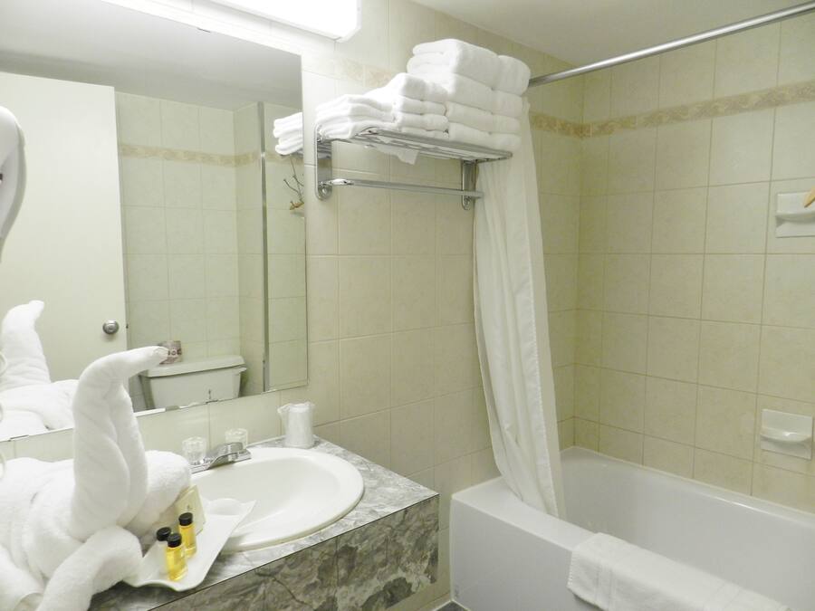 Un baño con lavamanos, espejo y bañera. Hay toallas apiladas en un perchero y una cortina de ducha.