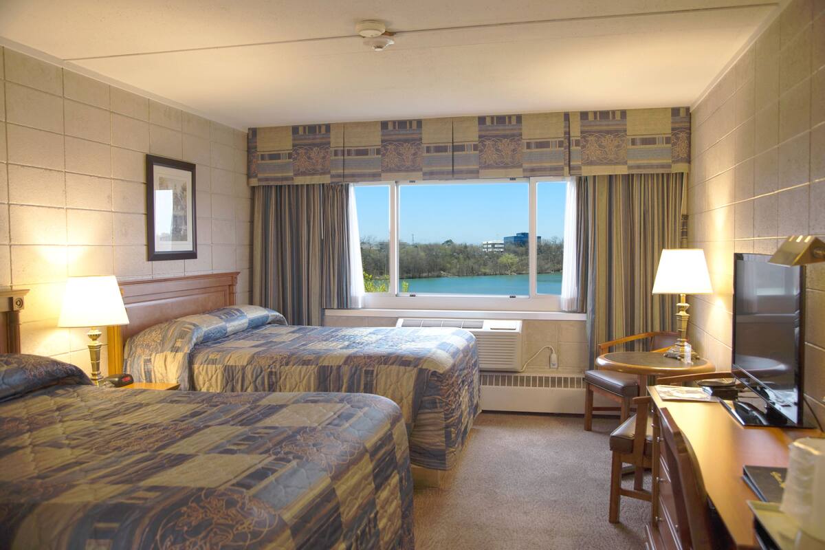 Camera d'albergo con due letti, una scrivania, una sedia, un televisore e un'ampia finestra vista mare.
