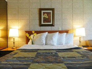 A hotel room with a bed, two bedside lamps, a vase with flowers, and a framed picture on the wall.