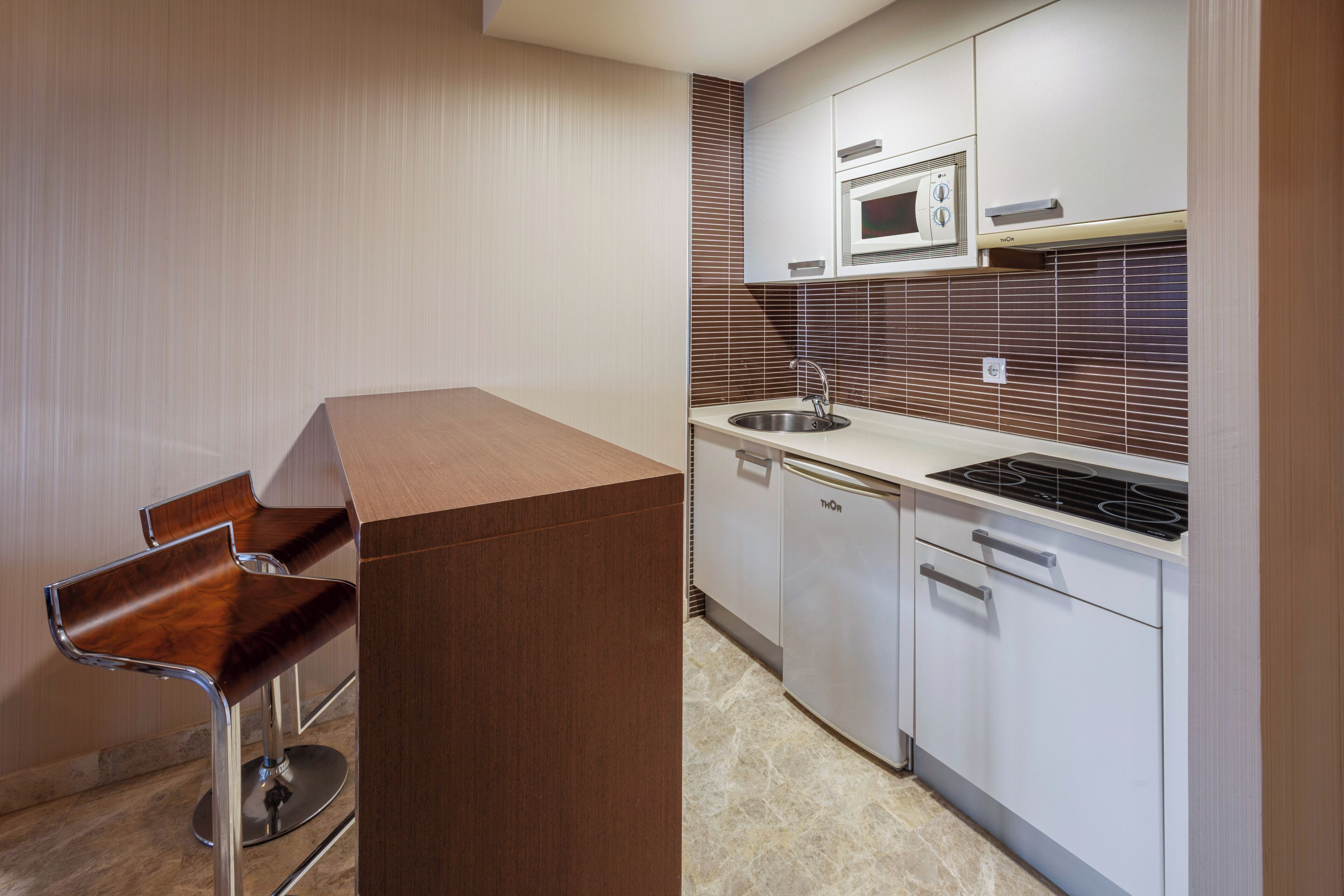 A modern kitchen with a microwave, stove, sink, and two bar stools.