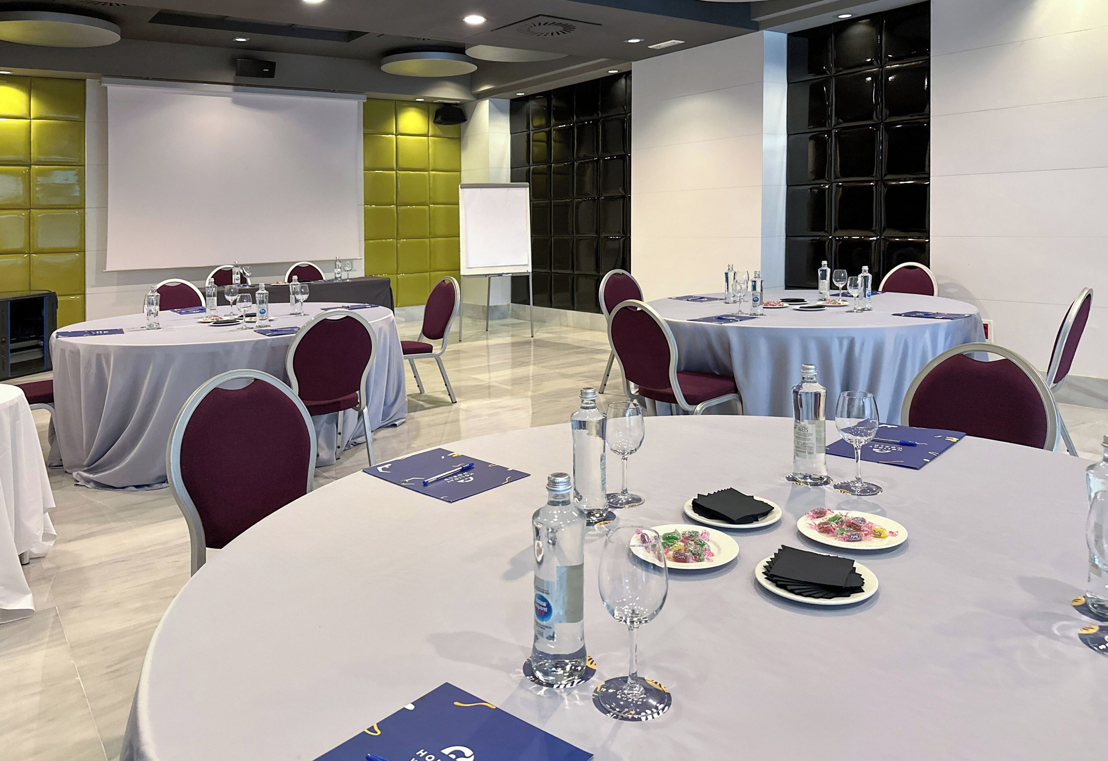 A conference room with round tables, chairs, and a presentation screen.
