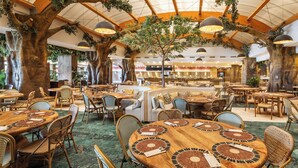 A restaurant with round wooden tables, wicker chairs, and a central tree. - Holiday World Polynesia Affiliated by Melia (Benalmádena)