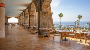 A terrace with tables and chairs, a view of the sea, and palm trees. - Holiday World Polynesia Affiliated by Melia (Benalmádena)