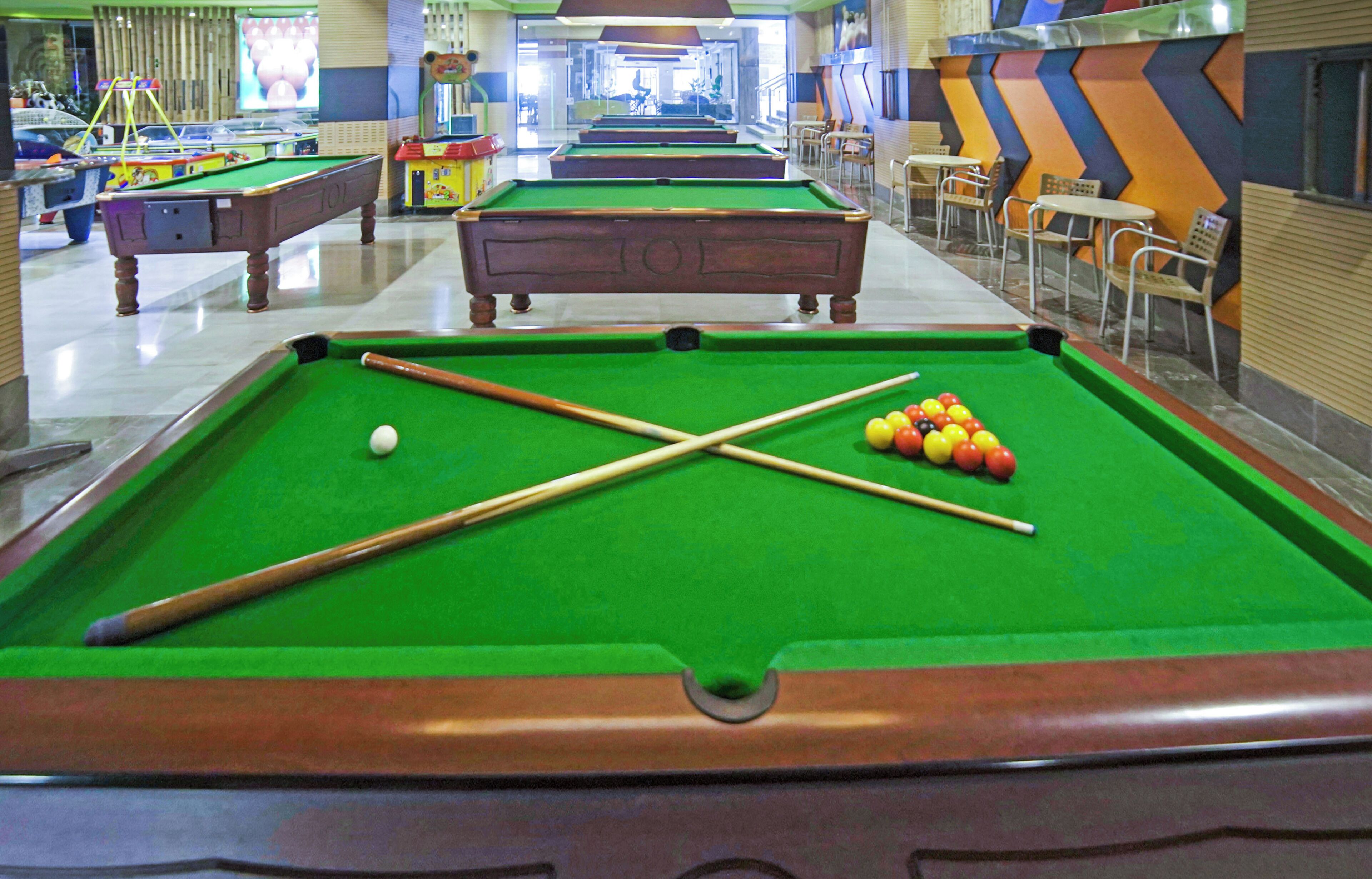 A pool table with balls and cues, a billiard table in the background, and a chevron-patterned wall.