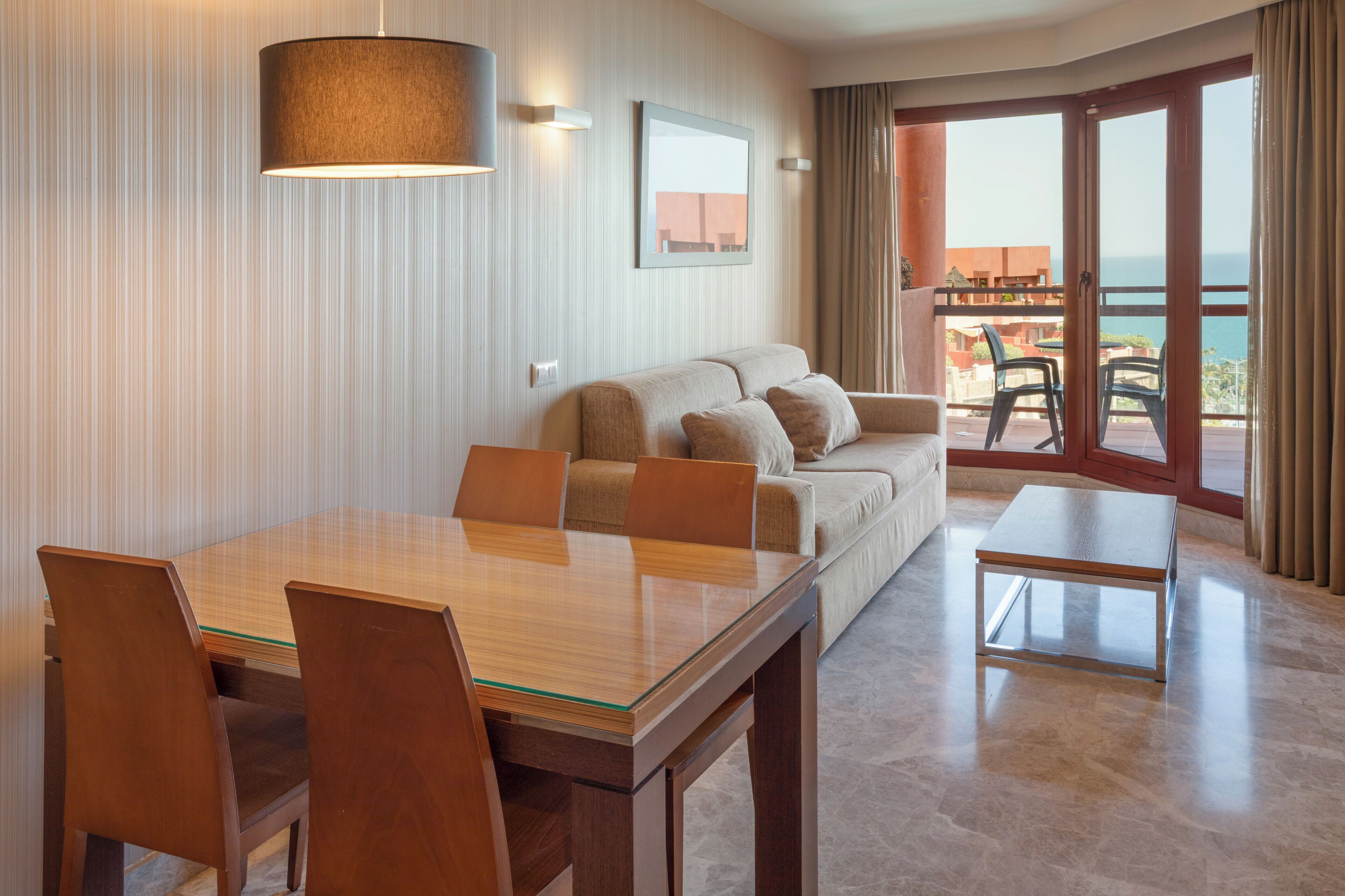 A modern hotel room with a dining area, a sofa, and a balcony with a view.