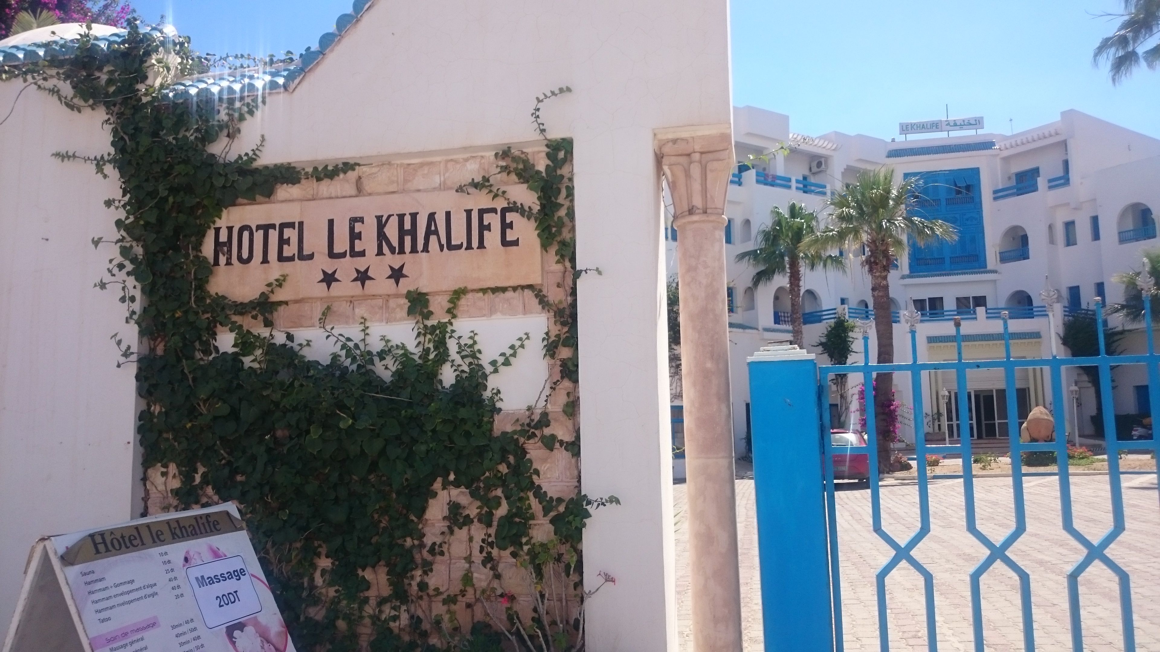 Entrada de un hotel con un letrero que dice 'HOTEL LE KHALIFE' y una puerta azul.