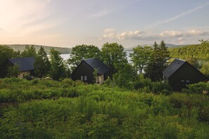 Three cabins with sloped roofs, surrounded by dense greenery and a lake in the background. - Duchesnay - SEPAQ (Sainte-Catherine-de-la-Jacques-Cartier)