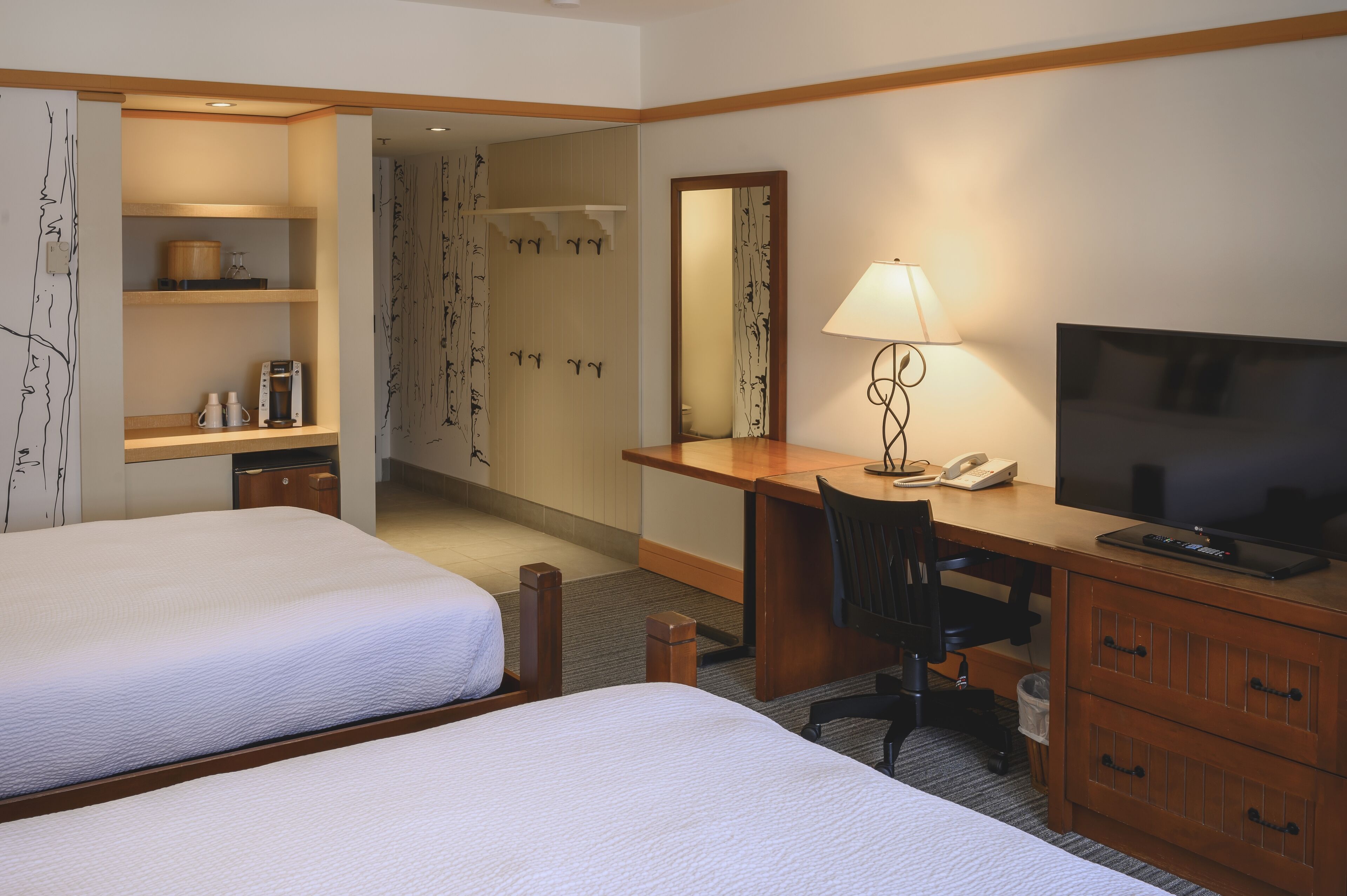 A hotel room with two beds, a desk with a chair, a television, and a bathroom visible in the background.