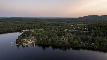 An aerial view of a lakeside property with a dock, surrounded by dense forest and hills in the background.