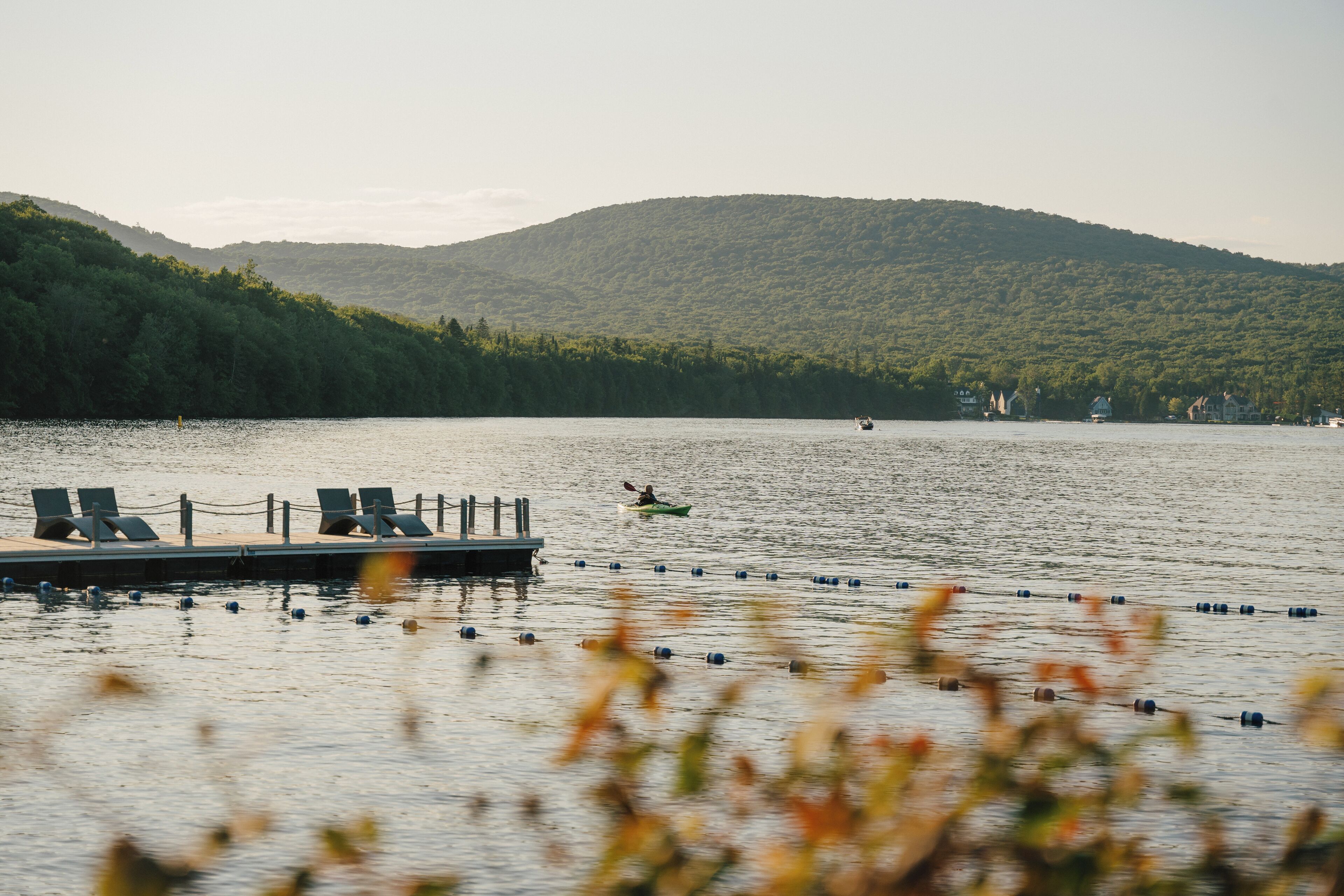 A calm lake with a dock and lounge chairs, surrounded by forested hills.