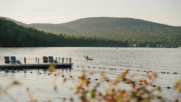 A calm lake with a dock and lounge chairs, surrounded by forested hills.