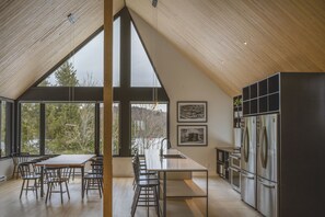 Une cuisine moderne dotée d’un grand îlot central, d’appareils électroménagers en acier inoxydable et offrant une vue sur l’extérieur.