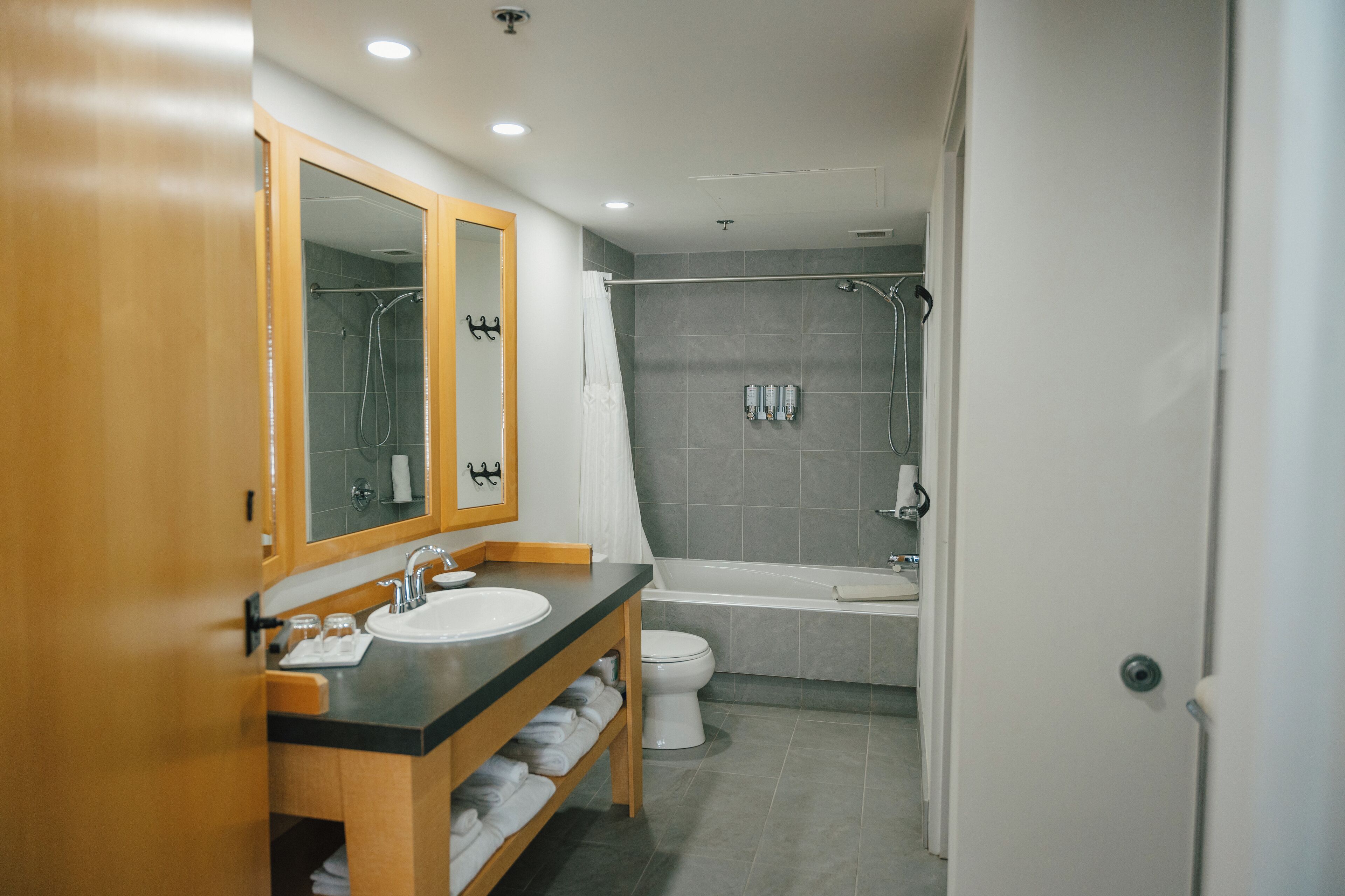 A modern bathroom with a wooden vanity, a large mirror, a bathtub, and a shower area.