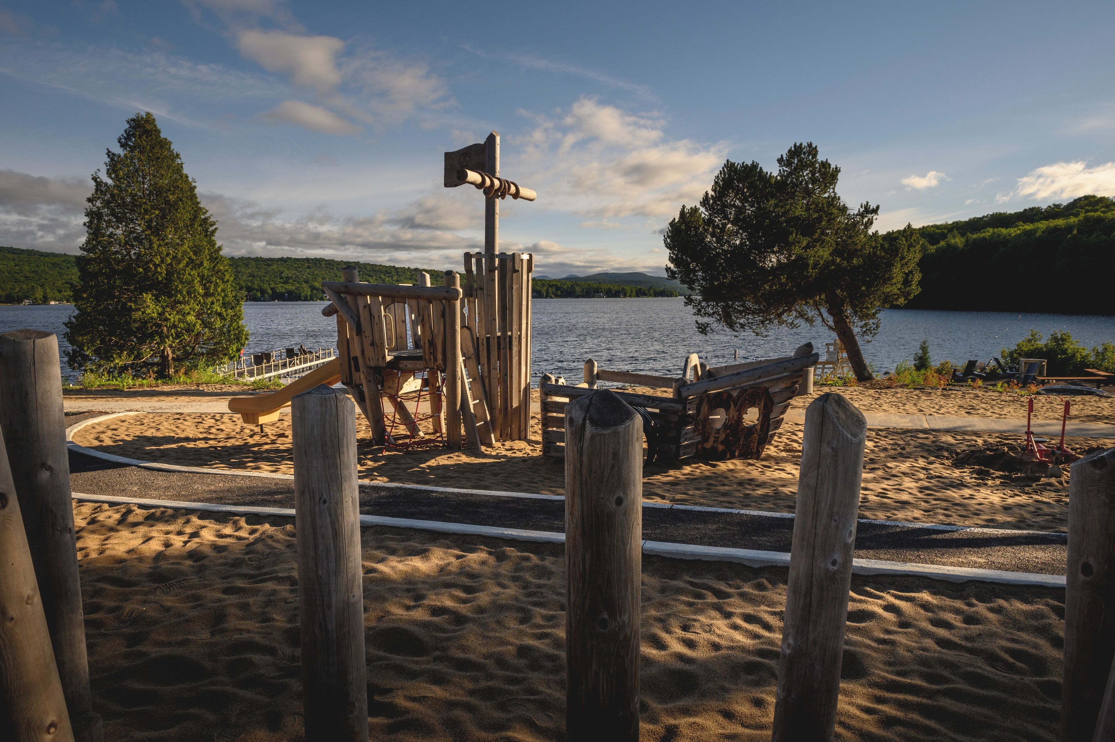 A sandy beach area with wooden play structures and a wooden post with a directional sign.
