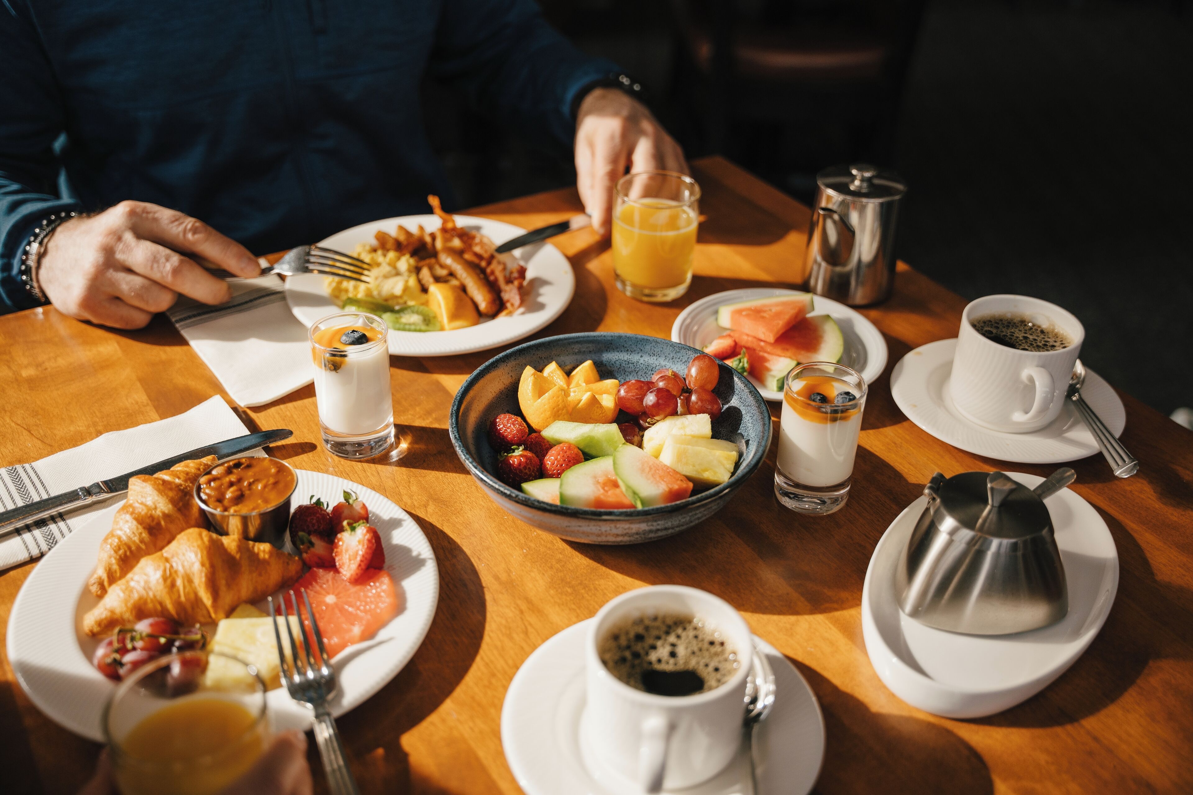A breakfast setting with croissants, fruit, coffee, and a hot drink on a wooden table.