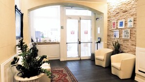 A hotel lobby with a reception desk, two seating areas, a large rug, and a stone wall with framed pictures. - Hotel Patavium (Padova)