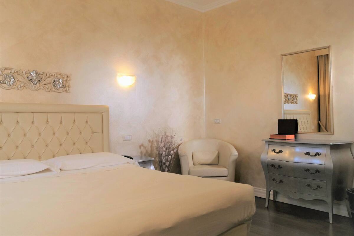 Une chambre à coucher avec un grand lit, une table de chevet, une chaise, une commode et un miroir fixé au mur.