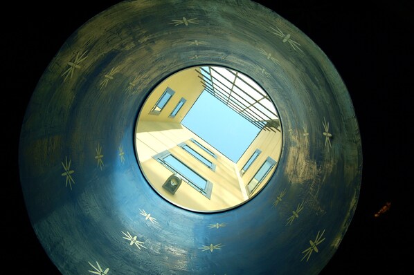 A circular architectural feature with a central skylight, reflecting a building with windows and a sloped roof.