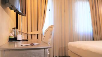 Ein Hotelzimmer mit einem Bett, einem Schreibtisch mit Kaffeemaschine, einem Sessel und Vorhängen.