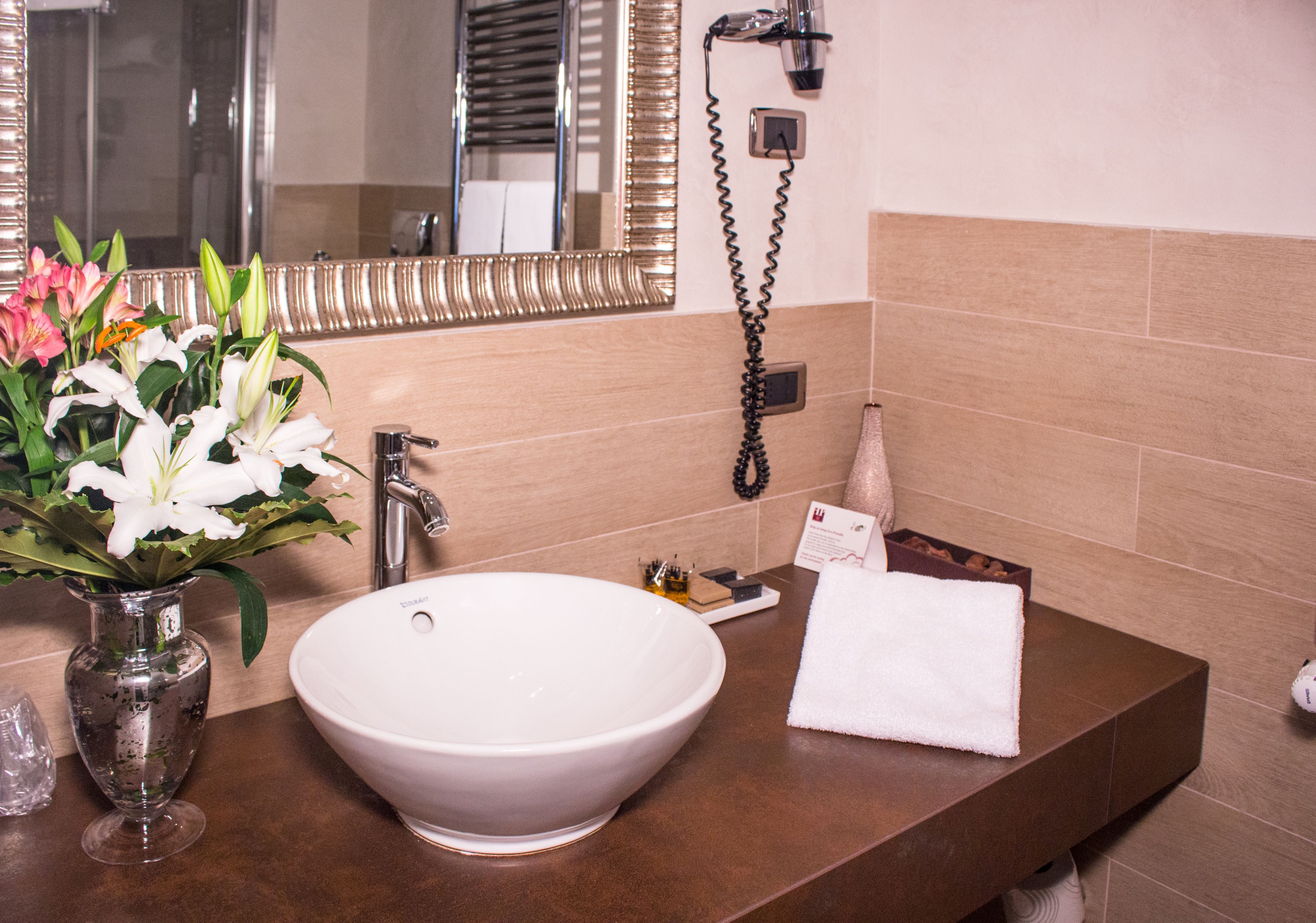 A bathroom with a large white sink, a mirror, and a vase of flowers.