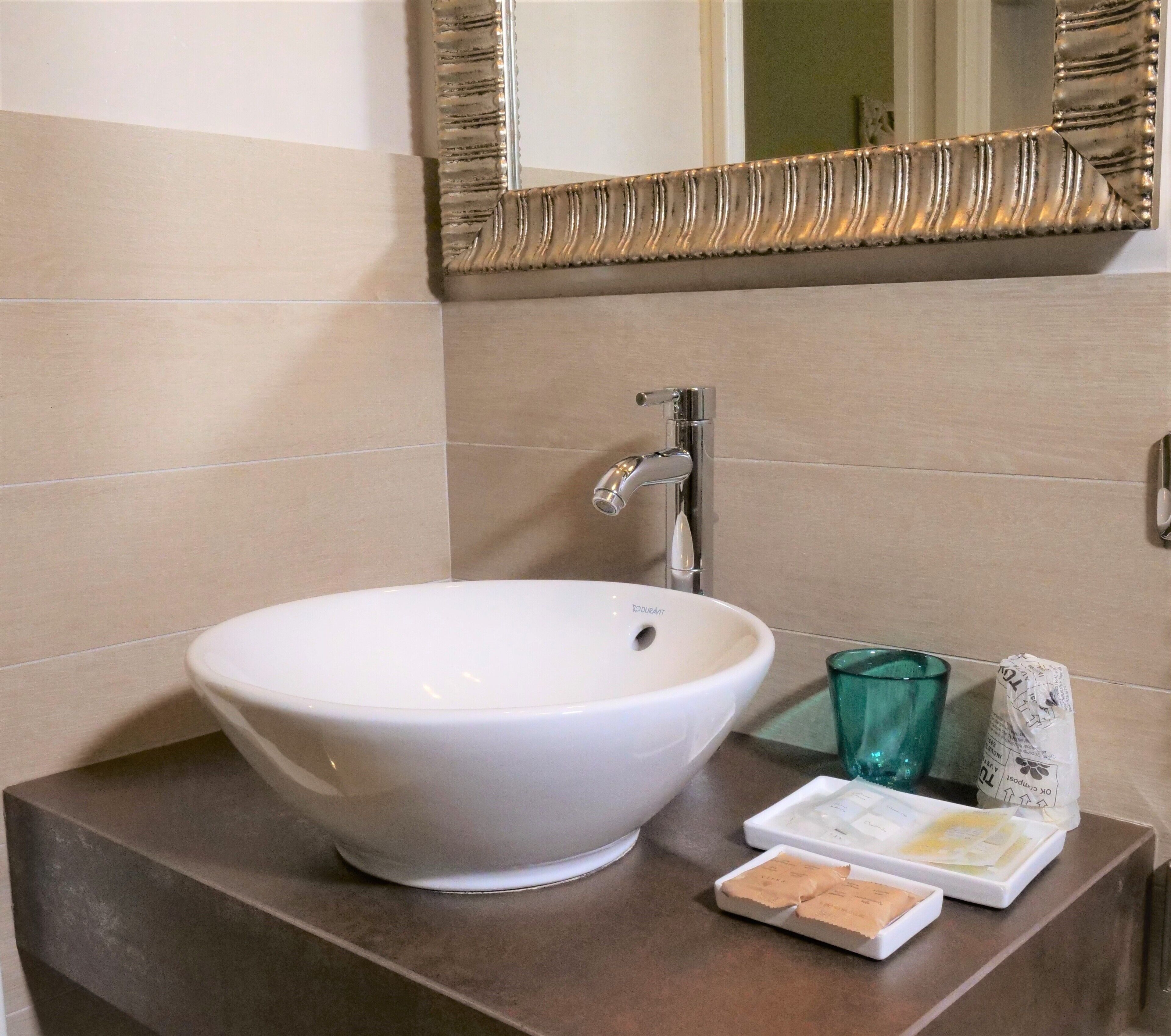 A bathroom with a white vessel sink, a mirror with a decorative frame, and toiletries on the counter.