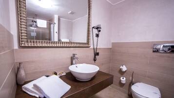 A modern bathroom with a large mirror, a white sink, a toilet, and a towel on the counter.