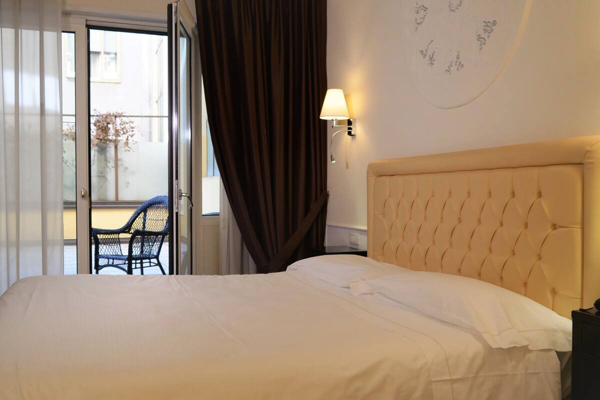 Une chambre d’hôtel avec un lit, une chaise, une lampe et une vue sur l’extérieur.