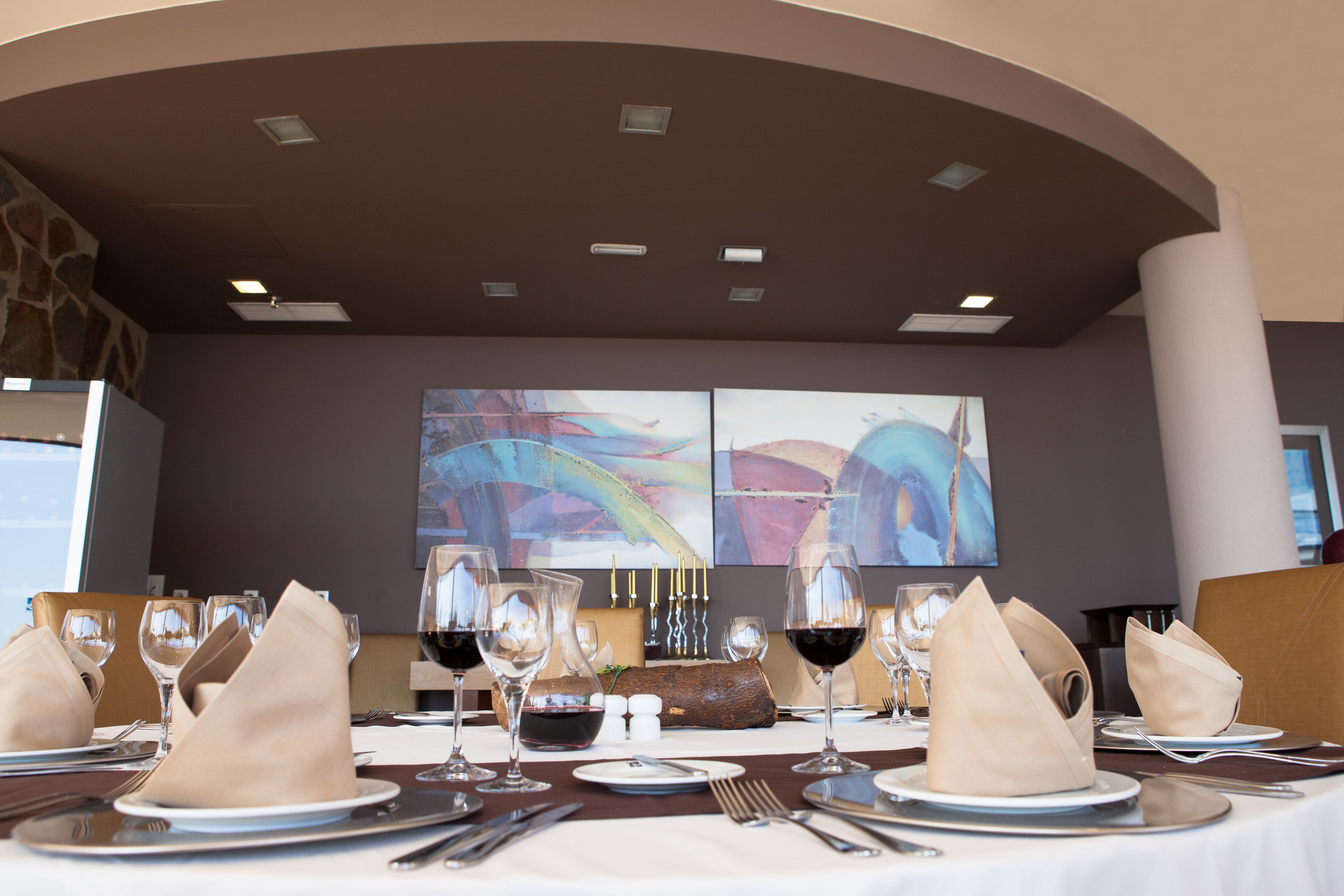 A dining table set with wine glasses, plates, and cutlery, with abstract art on the wall behind.