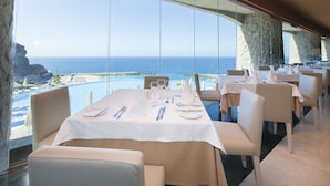 A dining area with tables set for two, overlooking a pool and the ocean. - Gloria Palace Royal Hotel & Spa (Mogan)