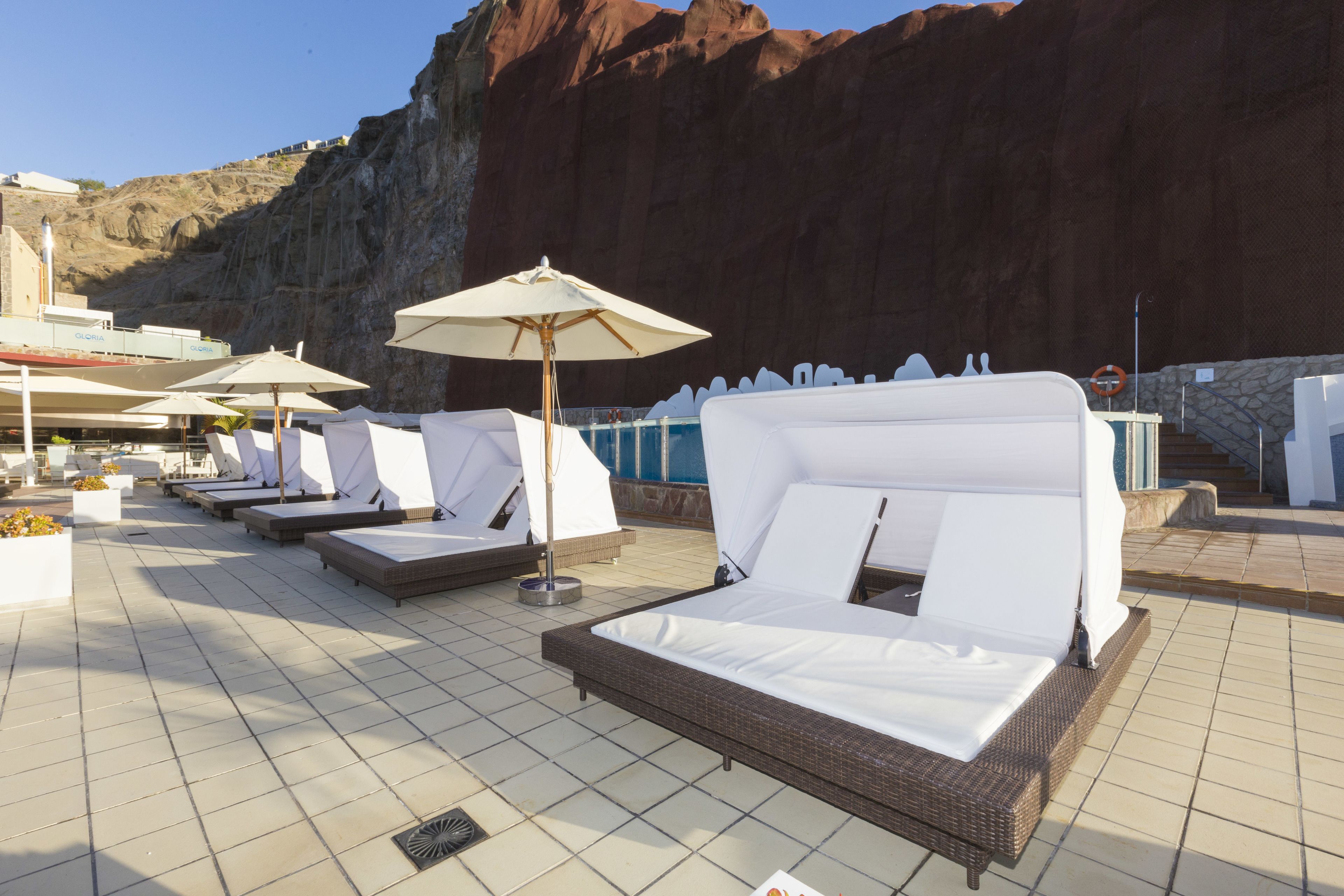 Un área de lounge en la azotea con tumbonas y sombrillas, con vistas a un paisaje rocoso.