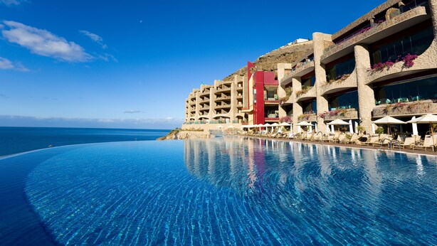 A hotel with a large infinity pool, a beach view, and a modern architectural design. - Gloria Palace Royal Hotel & Spa (Mogan)