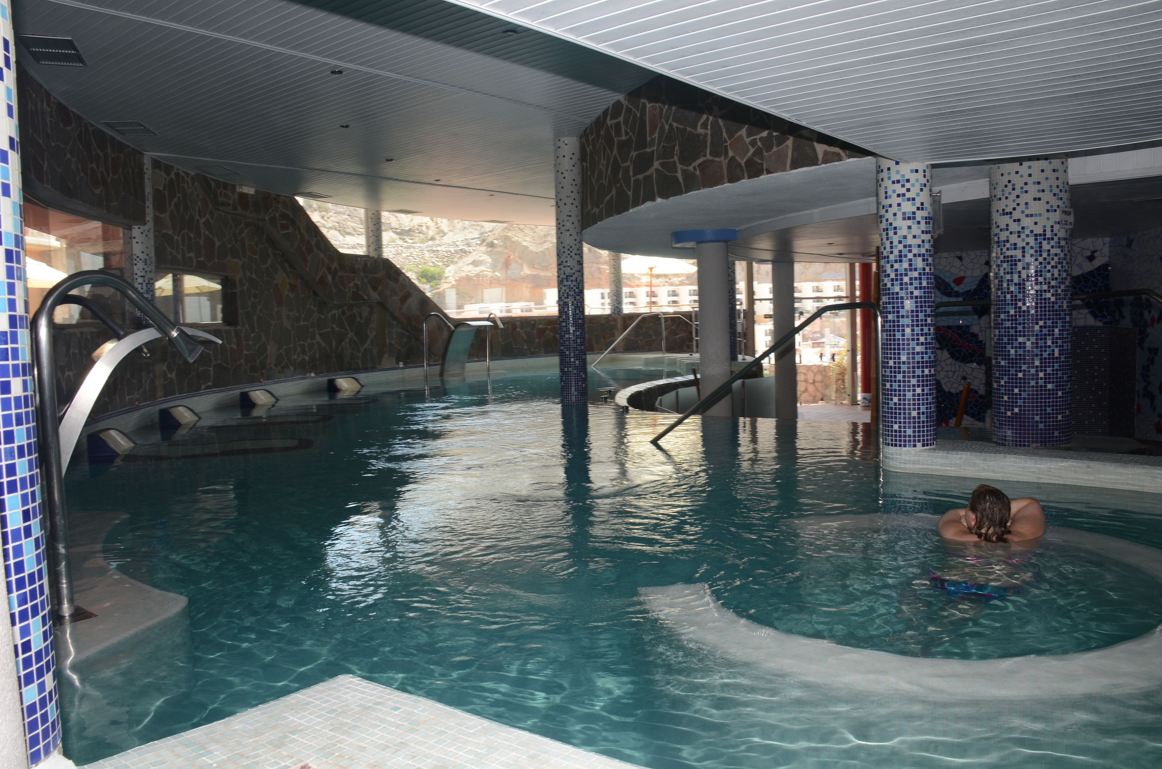 Una piscina interior con pared de piedra y una persona nadando.