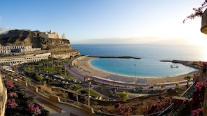 A coastal resort with a curved beach, a promenade, and a cliffside hotel. - Gloria Palace Royal Hotel & Spa (Mogan)