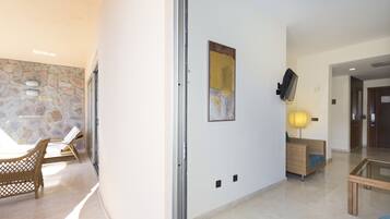 A modern lobby with a stone wall, wicker furniture, a glass table, and a mounted TV.