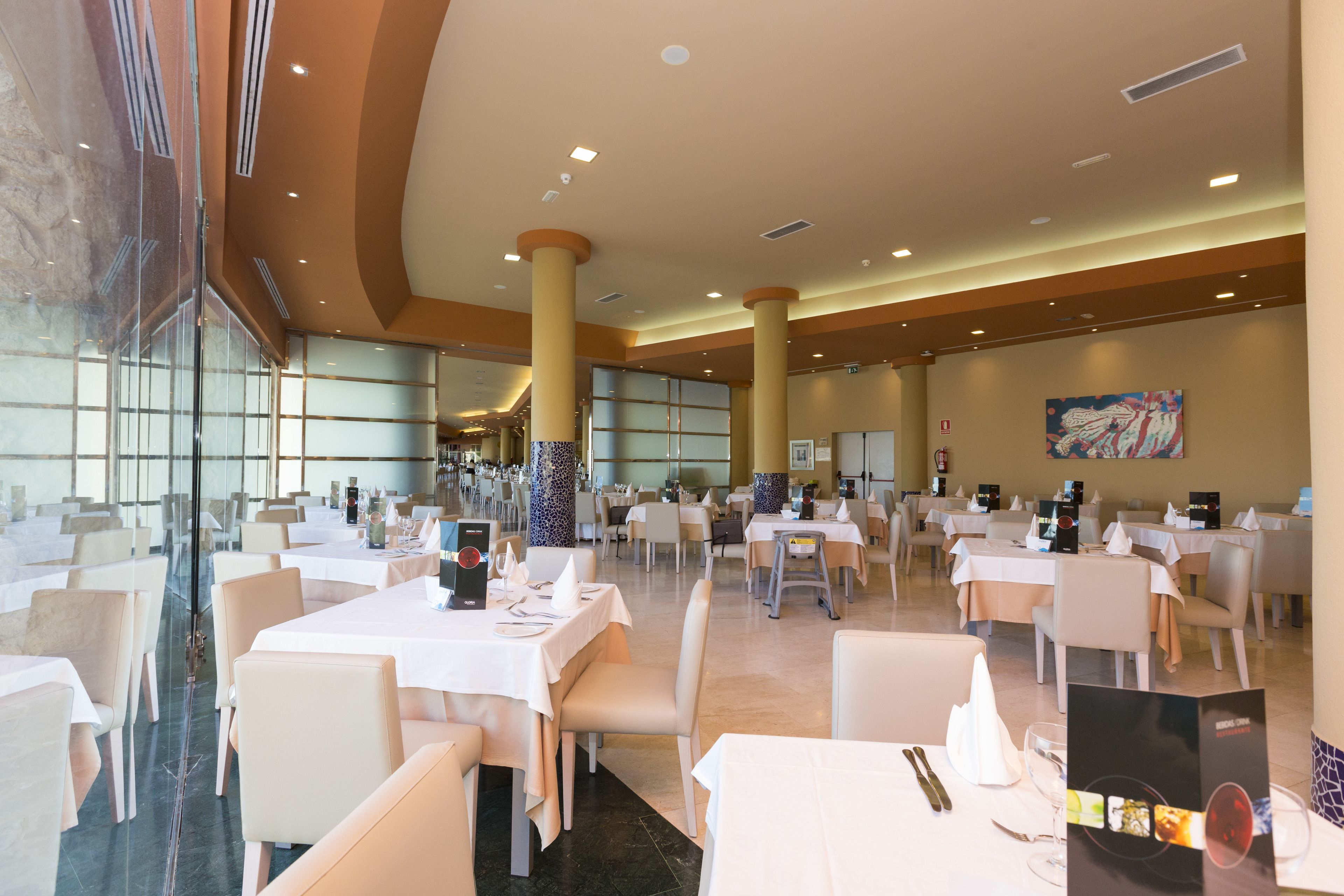 A spacious dining area with multiple tables and chairs, large windows, and a modern ceiling design.