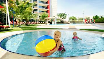 A pool area with a water slide, lounge chairs, and a building with balconies.