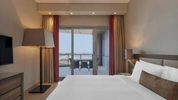 A hotel room with a large bed, a flat-screen TV, a bedside table, a lamp, and a view of the outdoors through a sliding door.