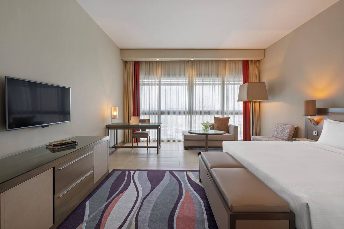 A hotel room with a bed, a desk, a chair, a television, and a window with curtains.