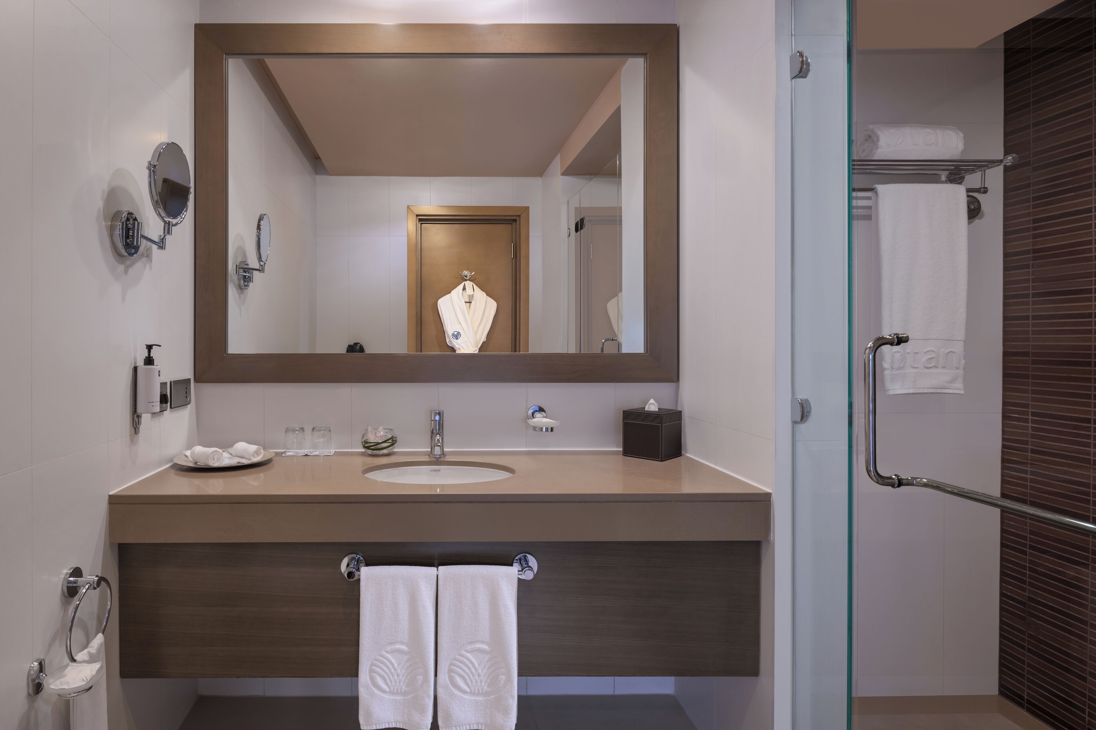 A modern bathroom with a large mirror, a sink, a towel rack, and a glass shower enclosure.