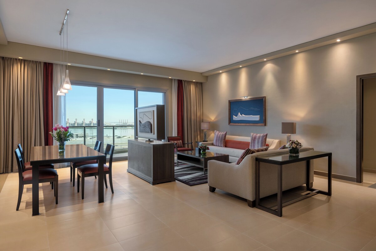 Een moderne hotelkamer met een zithoek, een bank, een televisie en een groot raam met uitzicht over de stad.