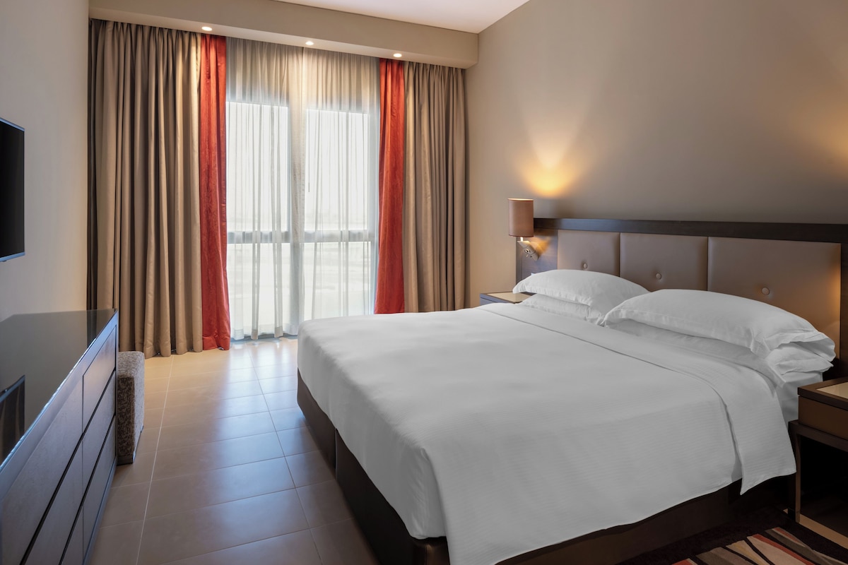 Une chambre d’hôtel avec un grand lit, une table de chevet, un téléviseur à écran plat et une fenêtre avec des rideaux.