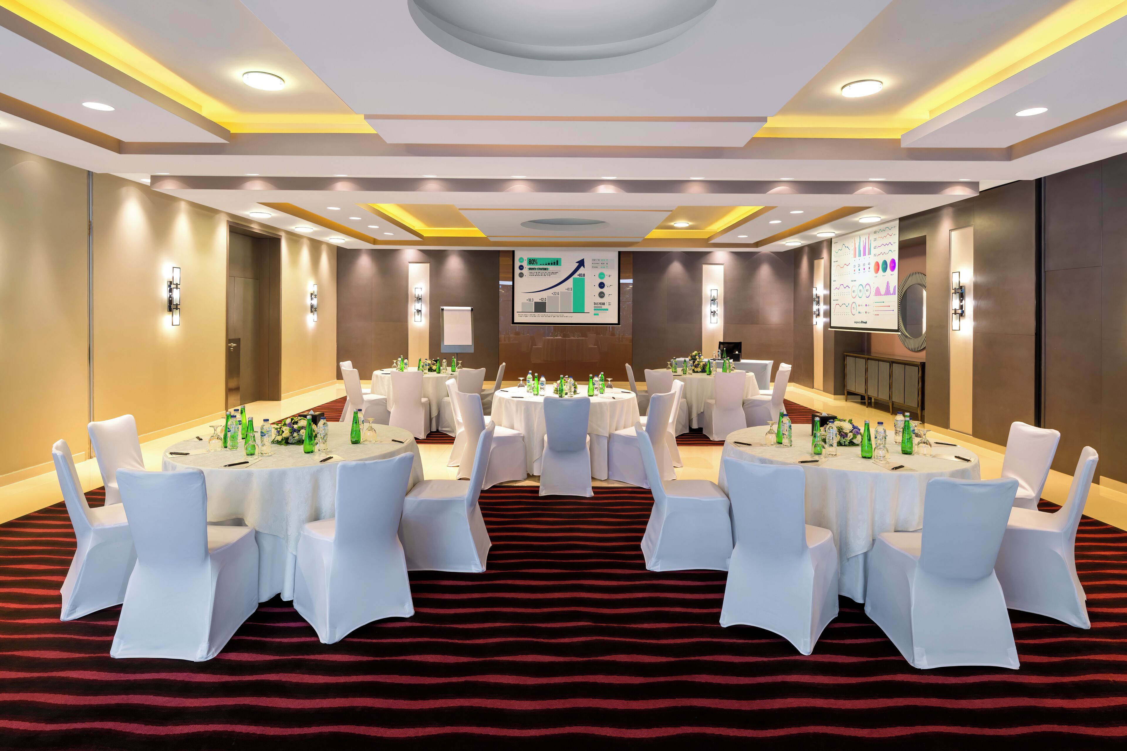 A conference room with round tables, white chairs, and a red carpet.