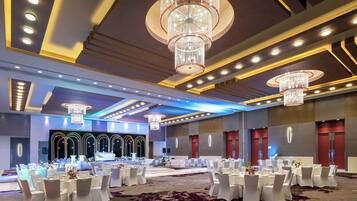 Un amplio salón de banquetes con mesas redondas, candelabros y un escenario.